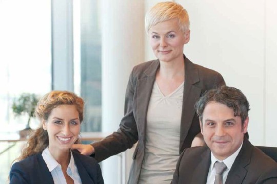 Das Gruppenbild zeigt drei Mitarbeiter (zwei Frauen und ein Mann) im Business-Outfit. Alle drei schauen lächelnd in die Kamera.